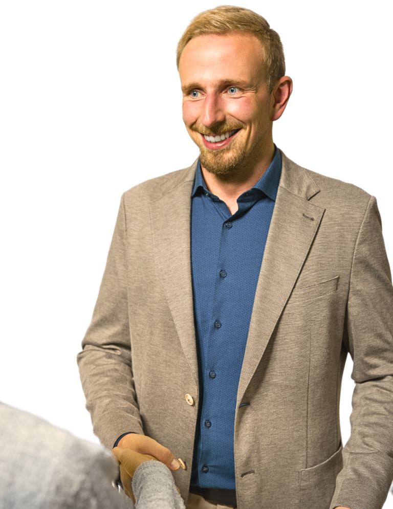 Mann mit blonder Frisur und lächelndem Gesicht, trägt blauen Hemd und hellen Anzug und schüttelt eine Hand.